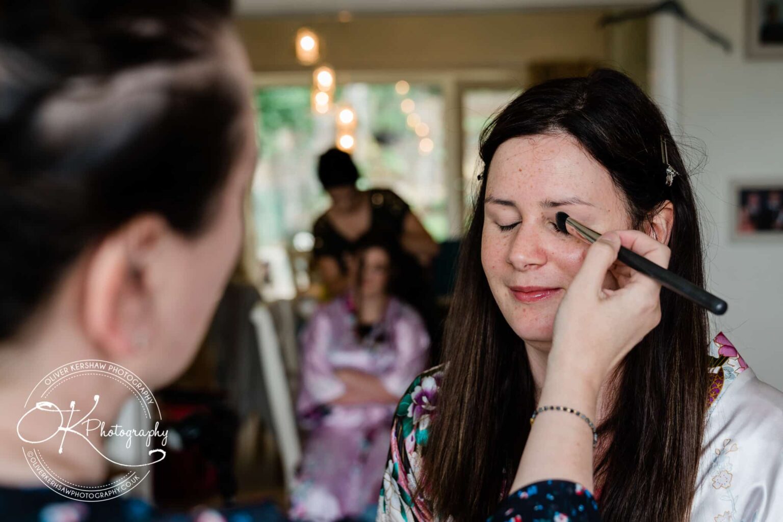 Person having makeup applied while another person works on hair in the background.