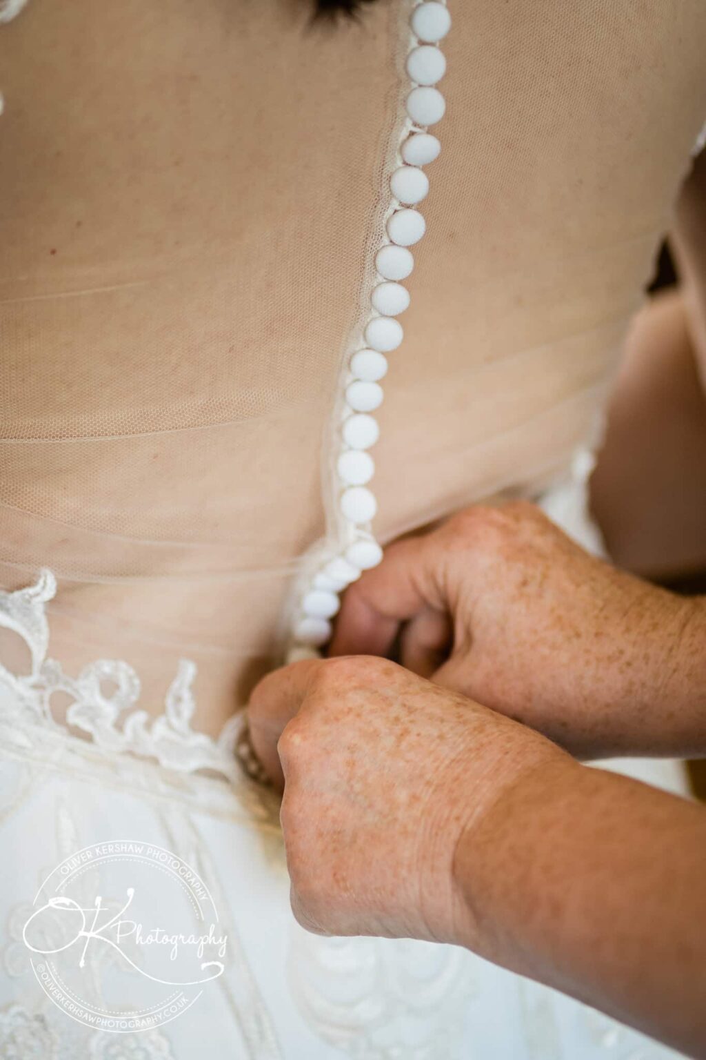 Hands fastening buttons on a lace wedding dress.