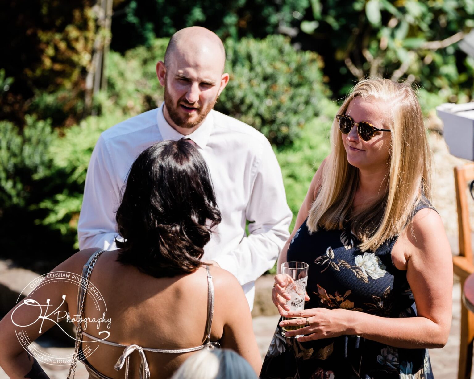 Three adults talking at an outdoor gathering, with two facing the camera and one has their back turned.