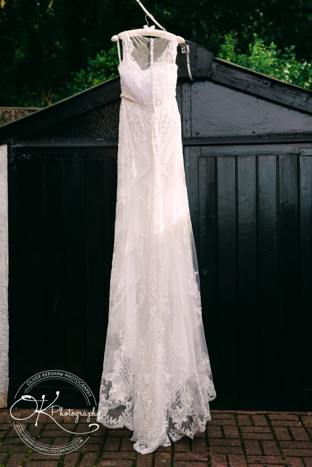 A white wedding dress hanging on a wooden hanger in front of a black door.