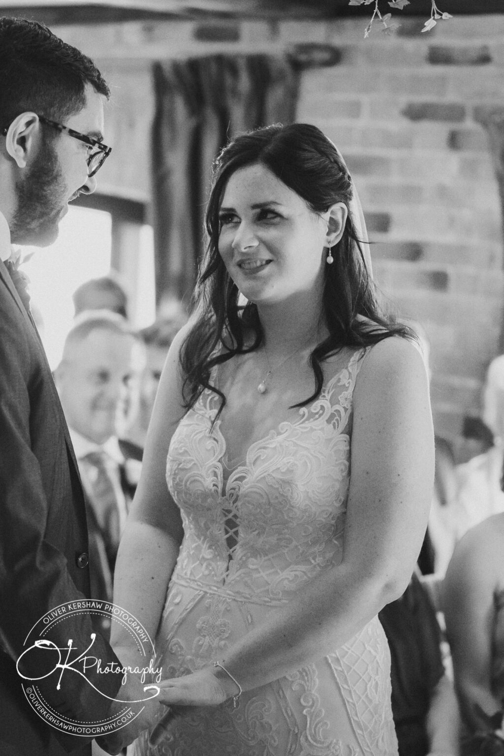 Bride and groom looking at each other during their wedding ceremony, with the bride wearing a lace wedding dress and holding the groom's hands.