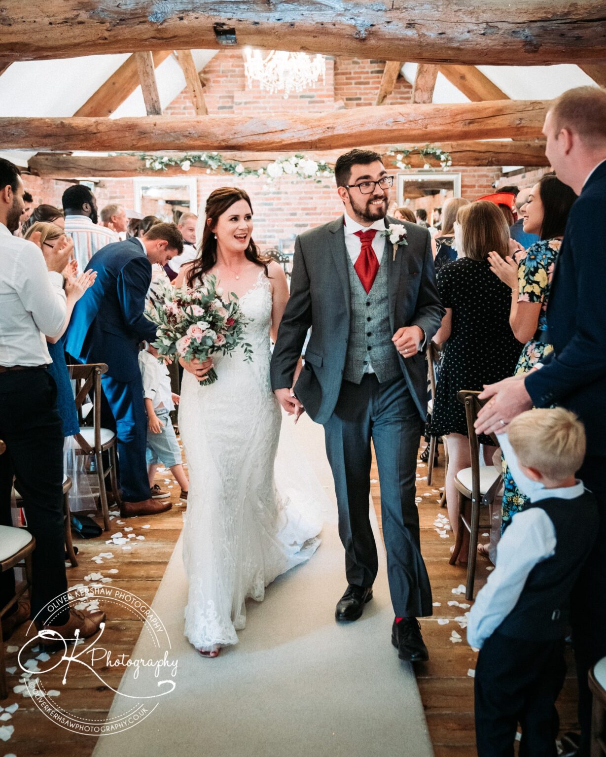 A bride and groom walking down the aisle at Swancar Farm, surrounded by guests applauding.