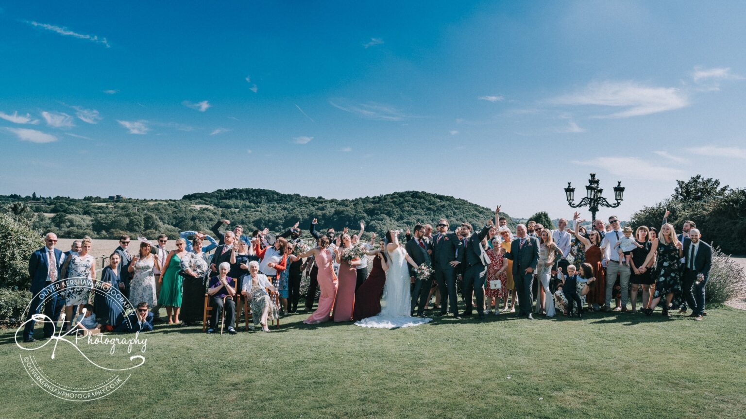 Wedding group photo at Swancar Farm against a scenic backdrop with guests celebrating under a clear blue sky.