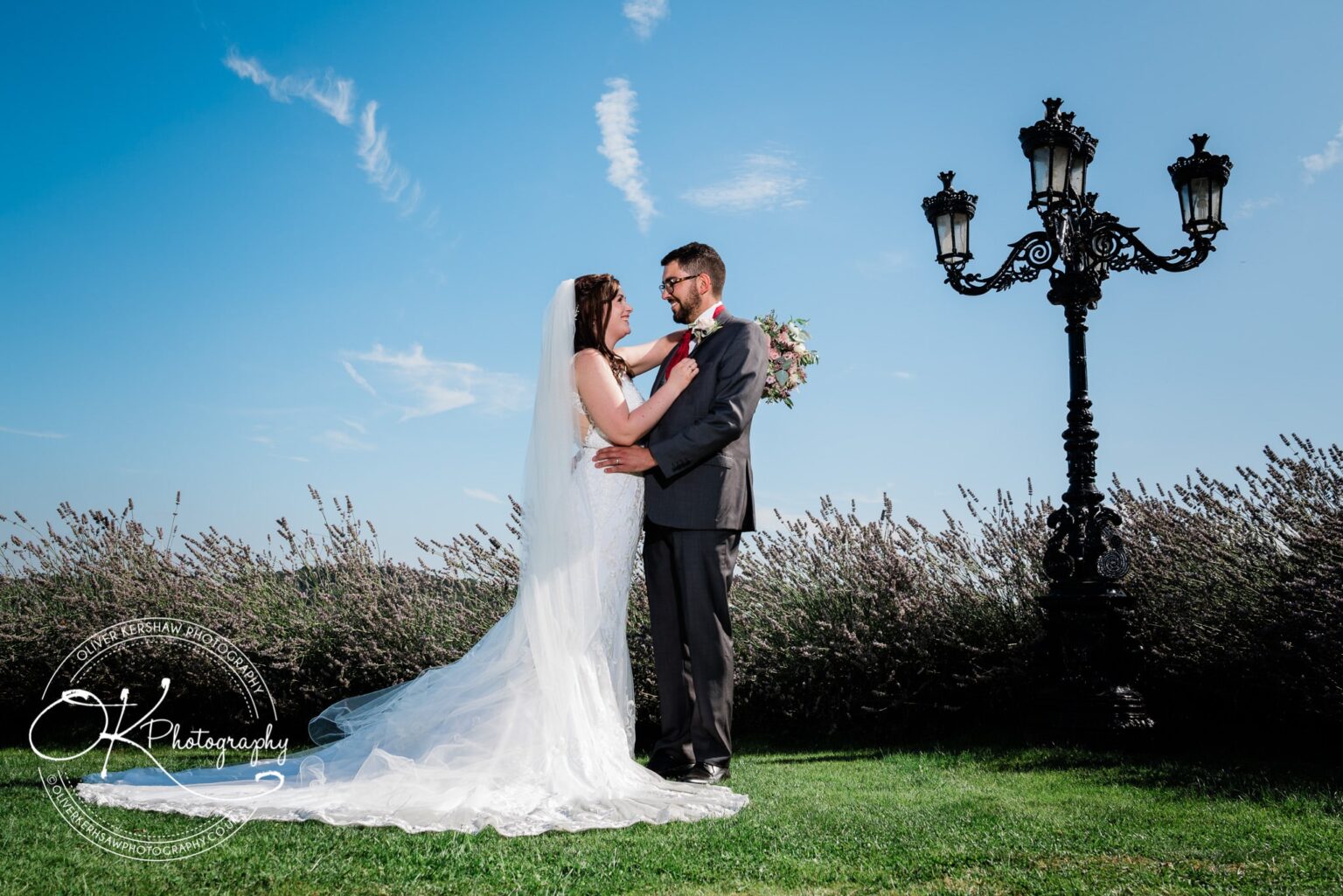 Bride and groom posing in front of a black vintage street lamp with a clear blue sky at Swancar Farm.