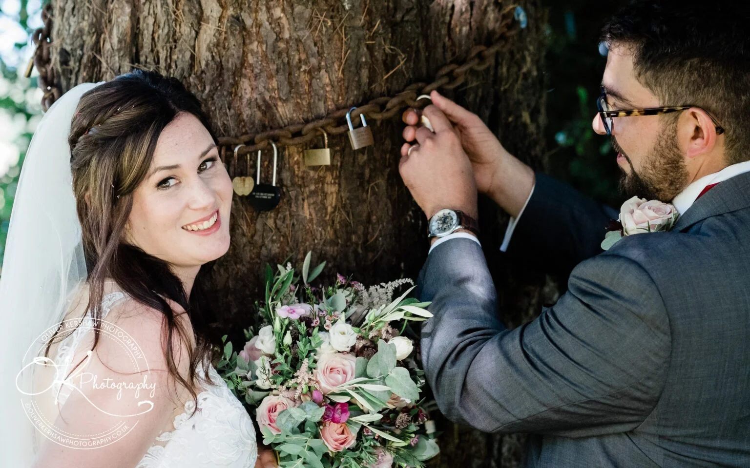 Bride and groom attaching a padlock to a chain around a tree.