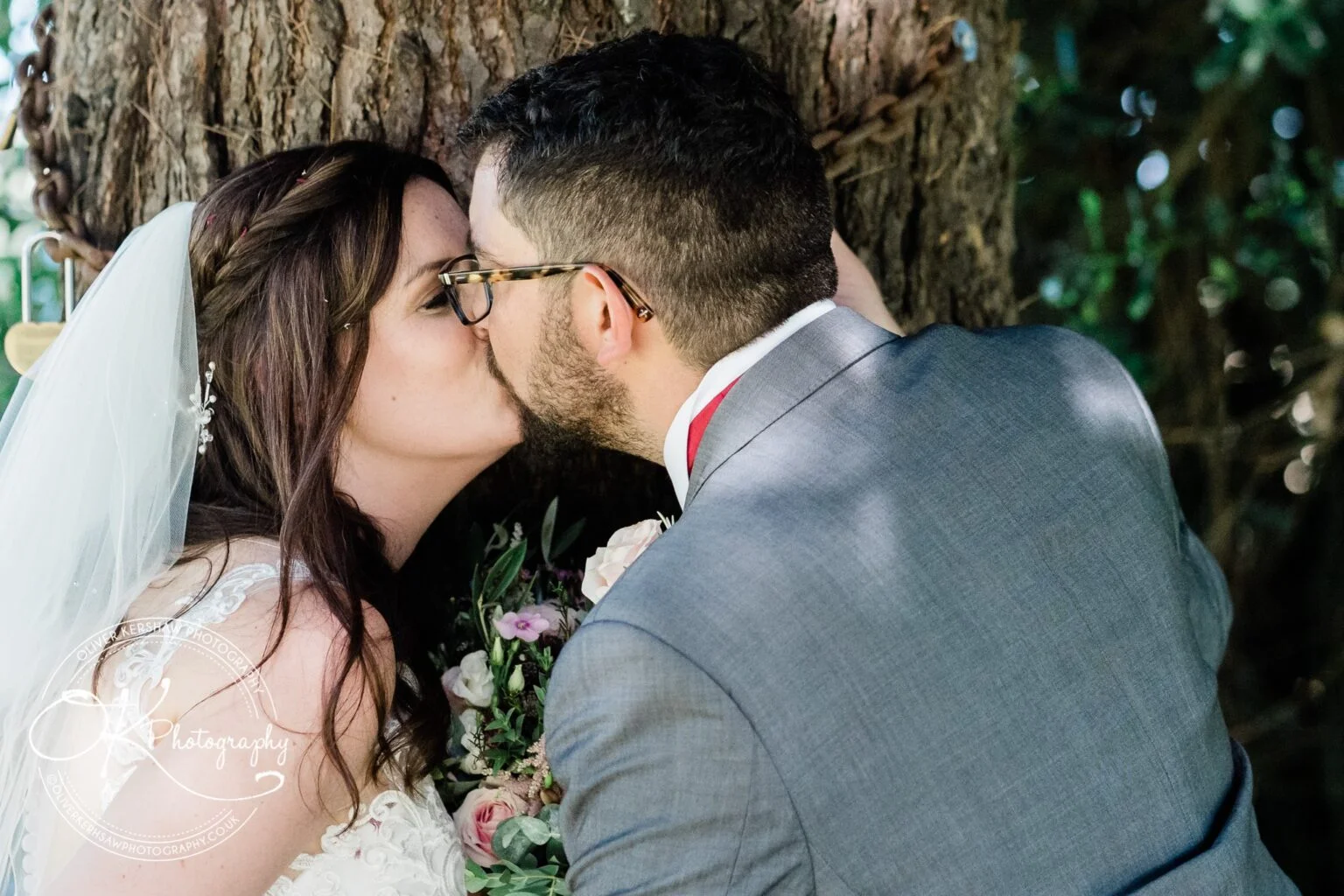 Bride and groom kissing in front of a tree at Swancar Farm.