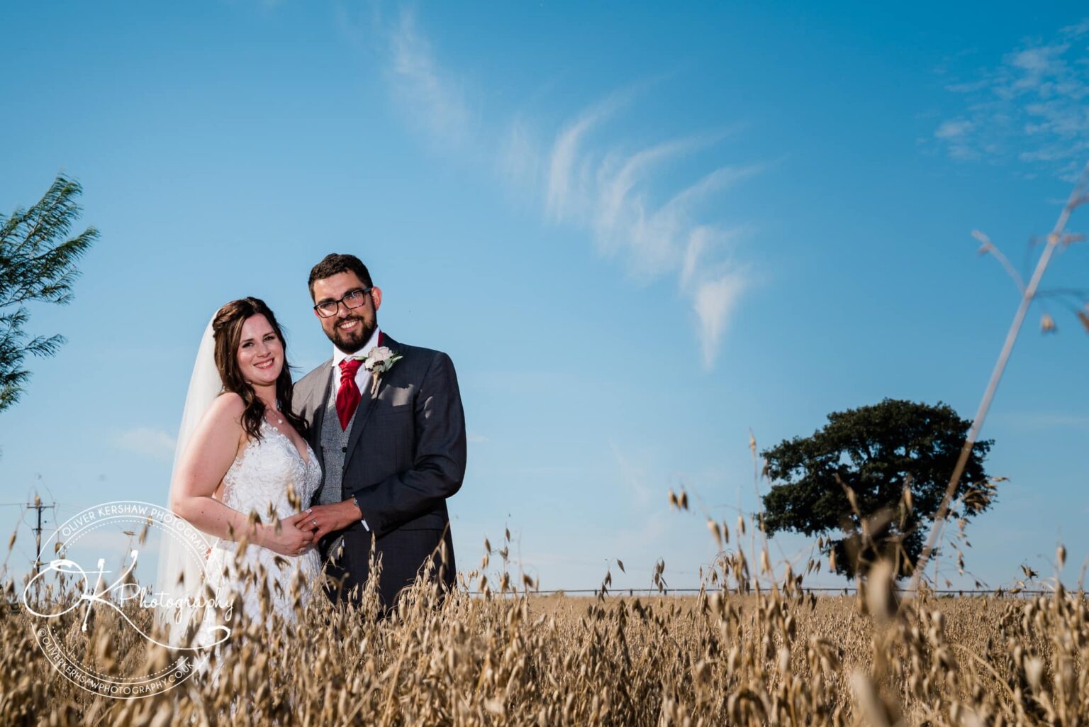 Bride and groom standing in a wheat field under a clear blue sky at Swancar Farm.