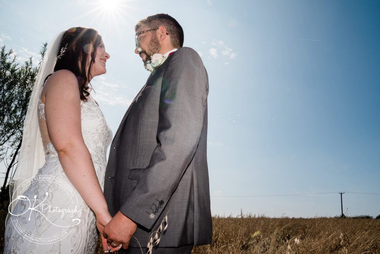Bride and groom holding hands and gazing at each other in a field on a sunny day.