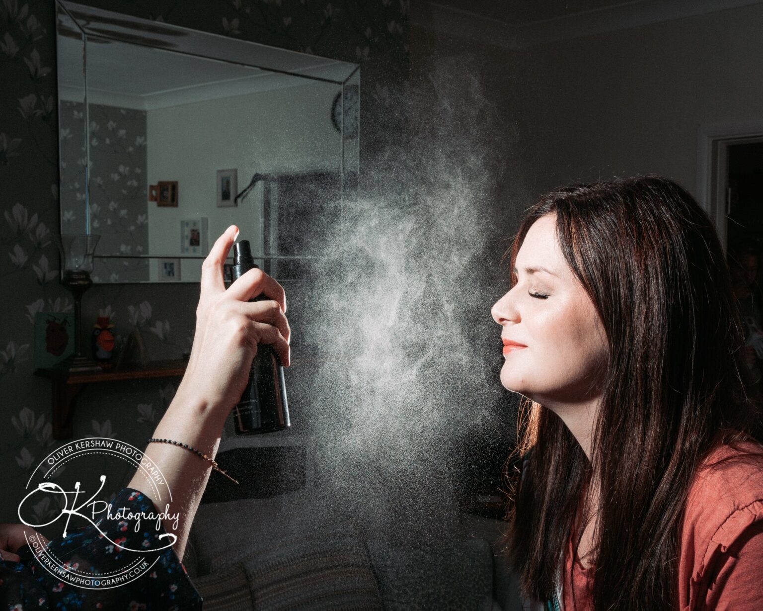 A woman with closed eyes having her face sprayed with mist by an unseen person.