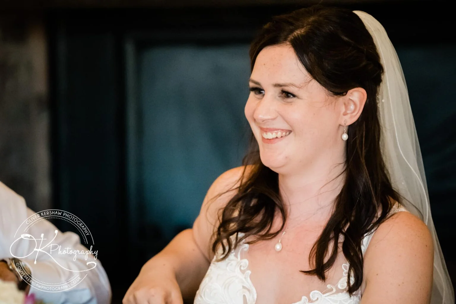 Bride smiling, wearing a veil and pearl earrings.