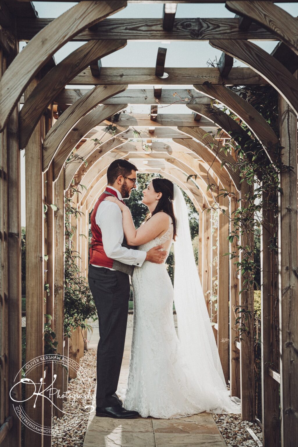 Bride and groom embracing under a wooden arched trellis at Swancar Farm.