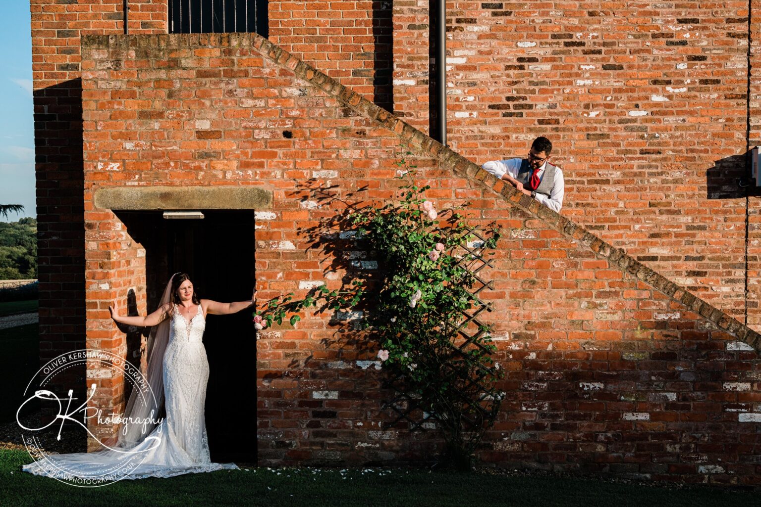 Bride standing in a doorway and groom leaning over a brick staircase, at Swancar Farm.