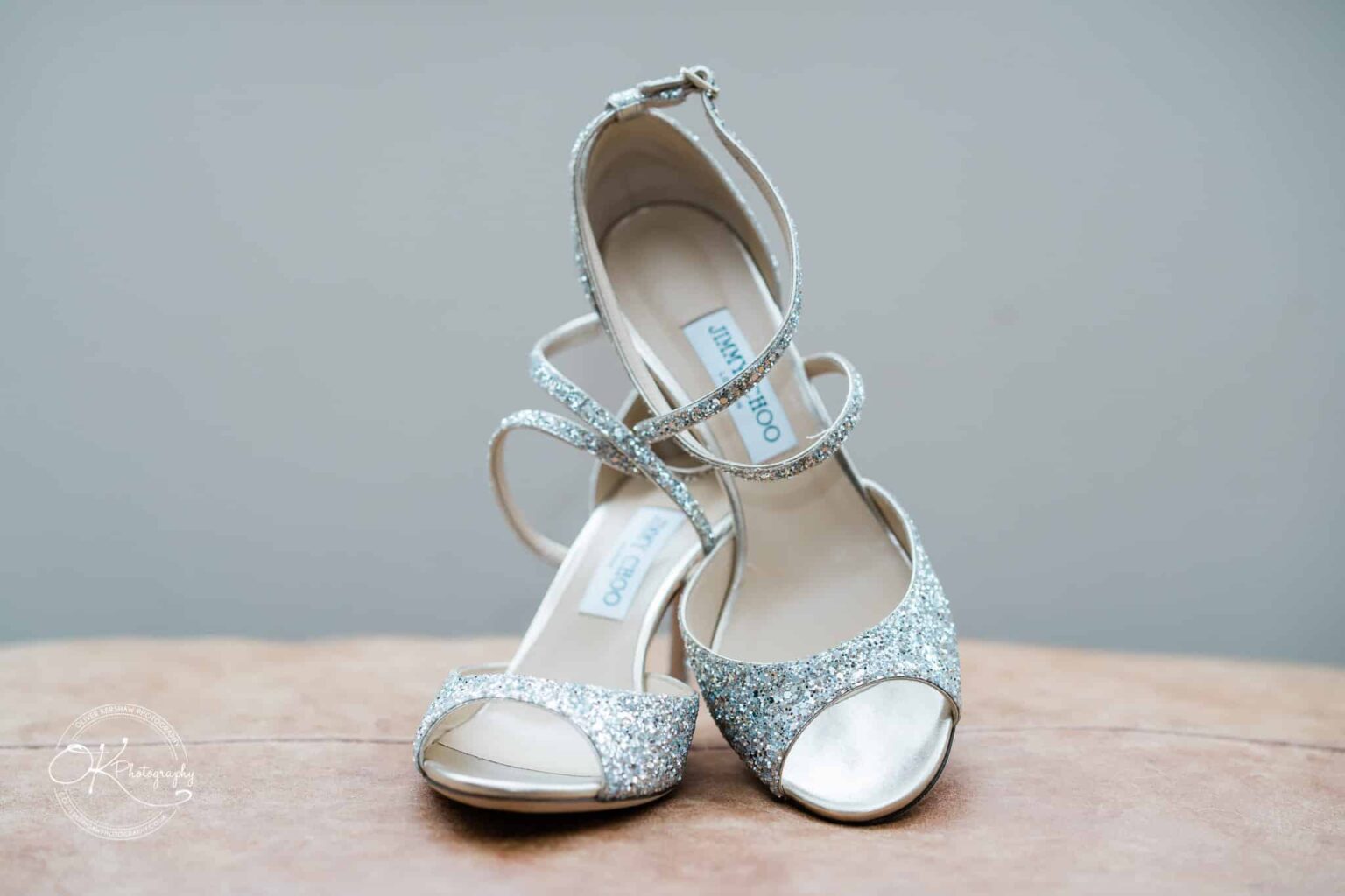 Silver glittery high-heeled sandals on a neutral background.