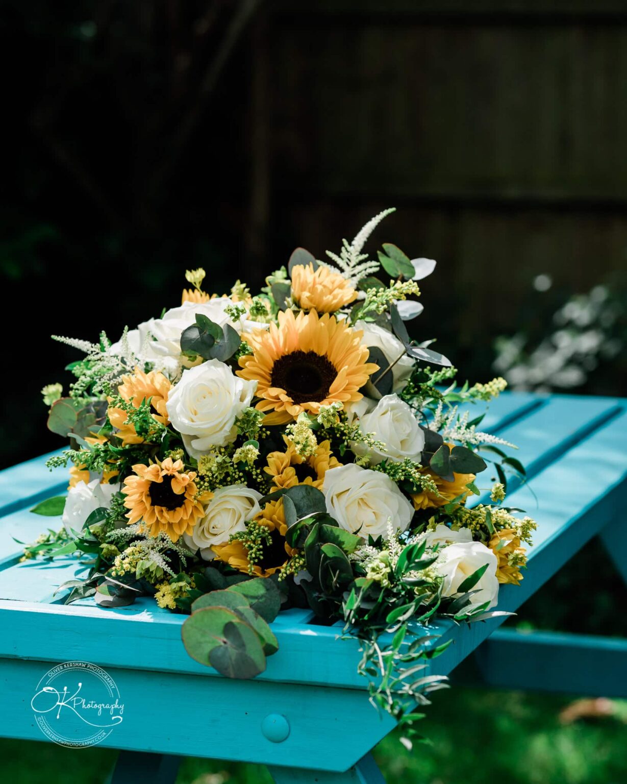 A bouquet of sunflowers and white roses on a light blue wooden table.