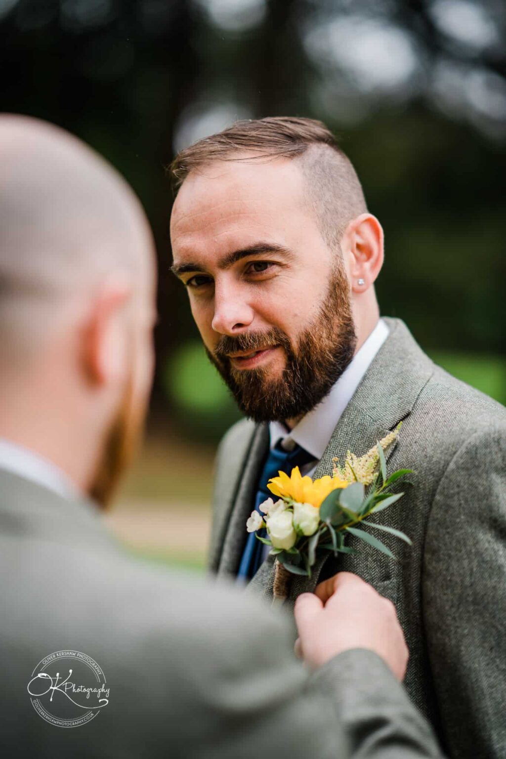 A man in a suit getting a boutonnière adjusted, with focus on his face and the flower arrangement.