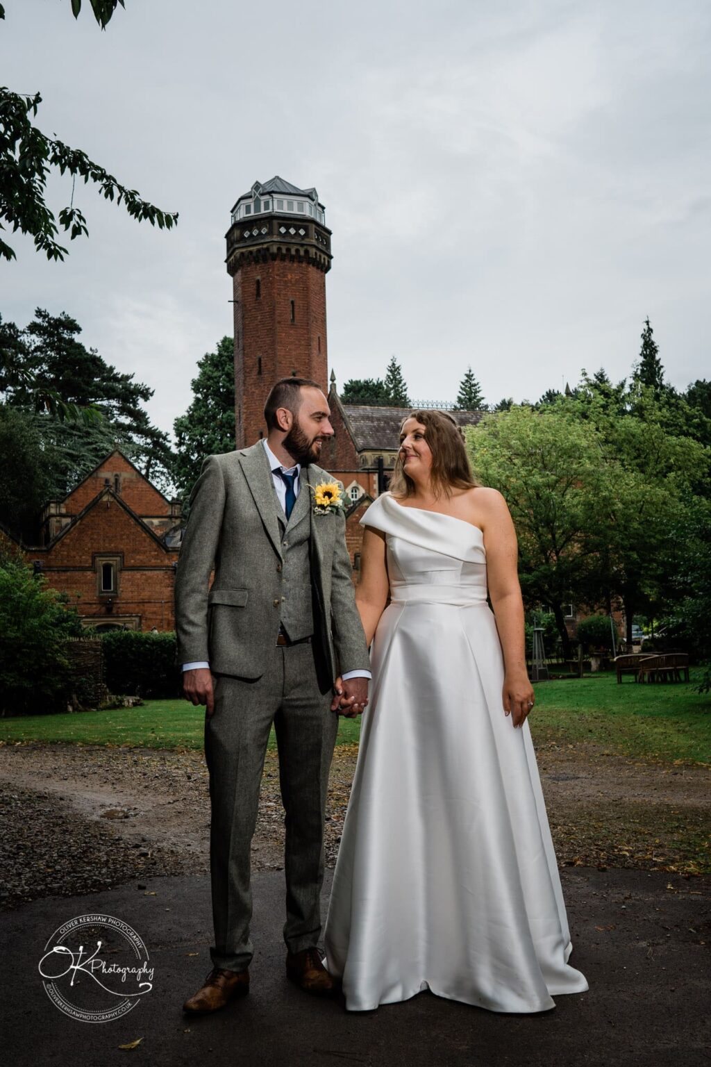 Bride and groom holding hands in front of a historic brick building with a tall tower.