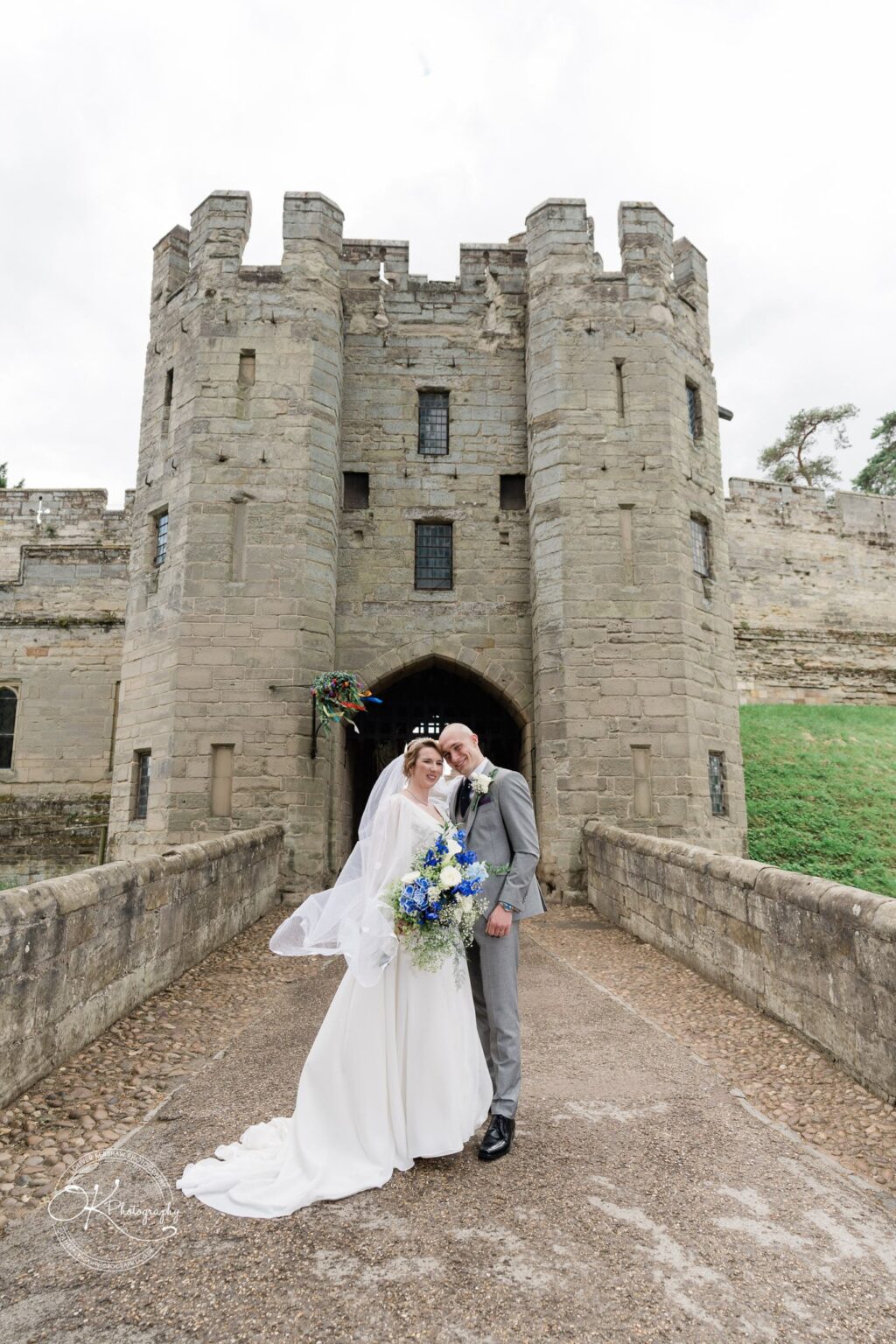 A newlywed couple posing outside the entrance of Warwick Castle.