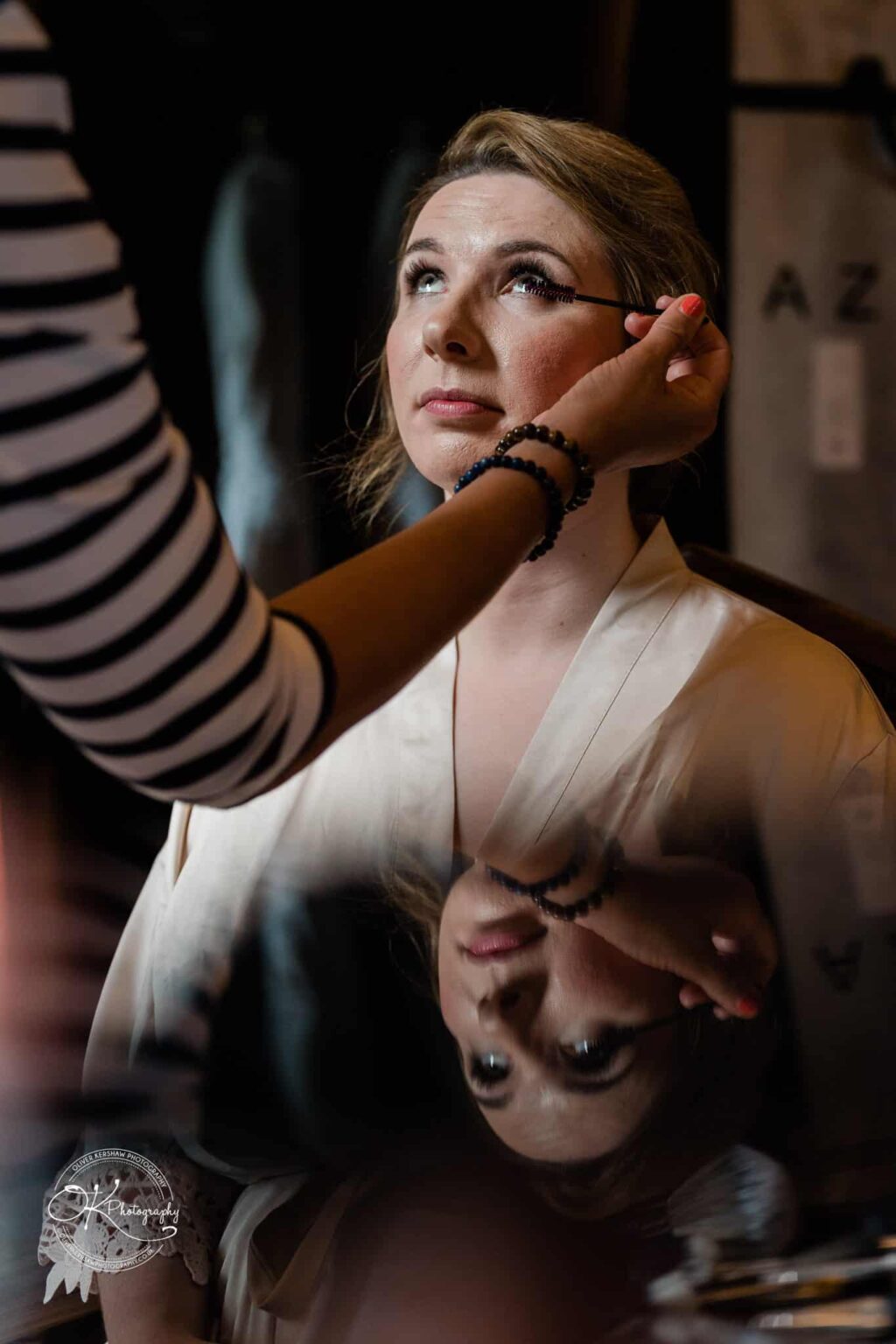 A woman getting her makeup done, with her reflection visible on a surface below.