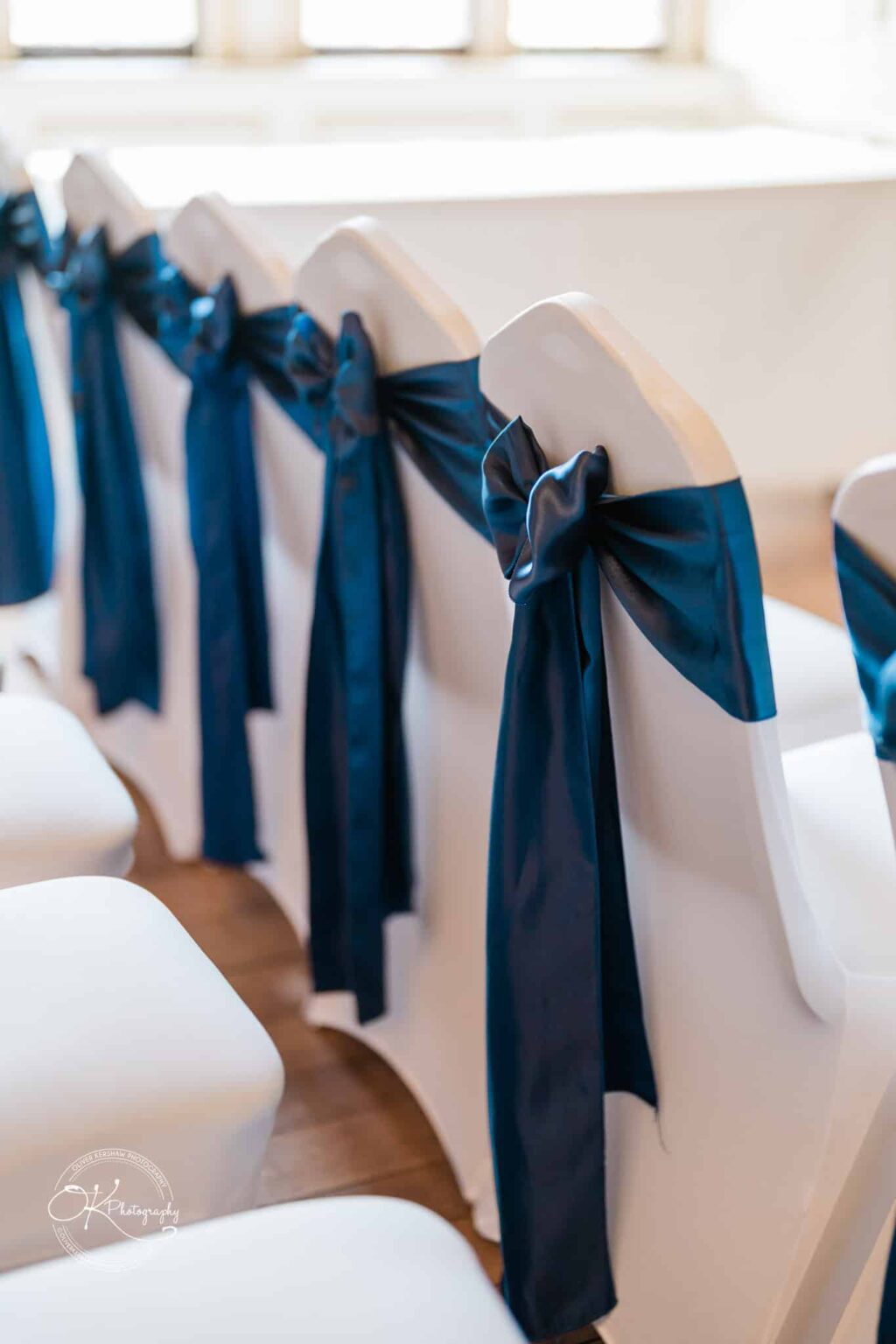 White chairs with dark blue satin bows on their backs, arranged in a row.