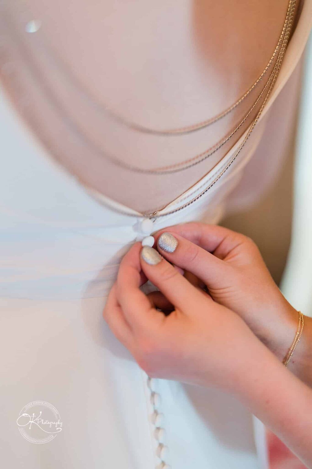 Hands fastening small buttons on the back of a wedding dress.