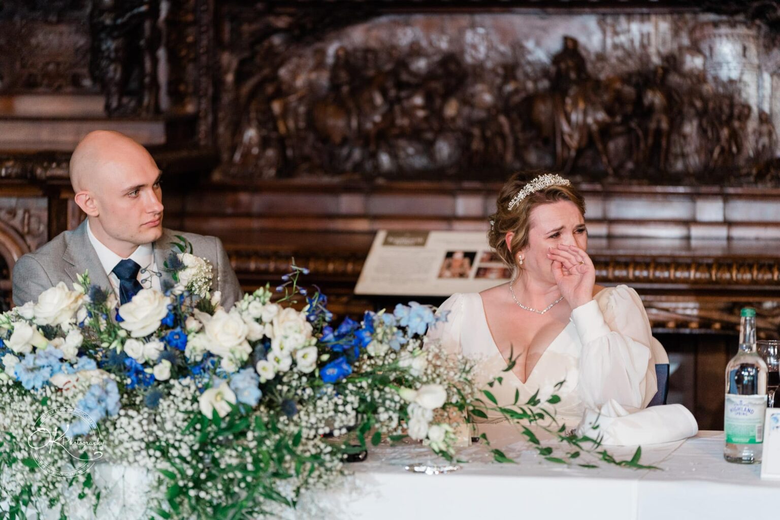 Bride and groom sitting at a table decorated with white and blue flowers.