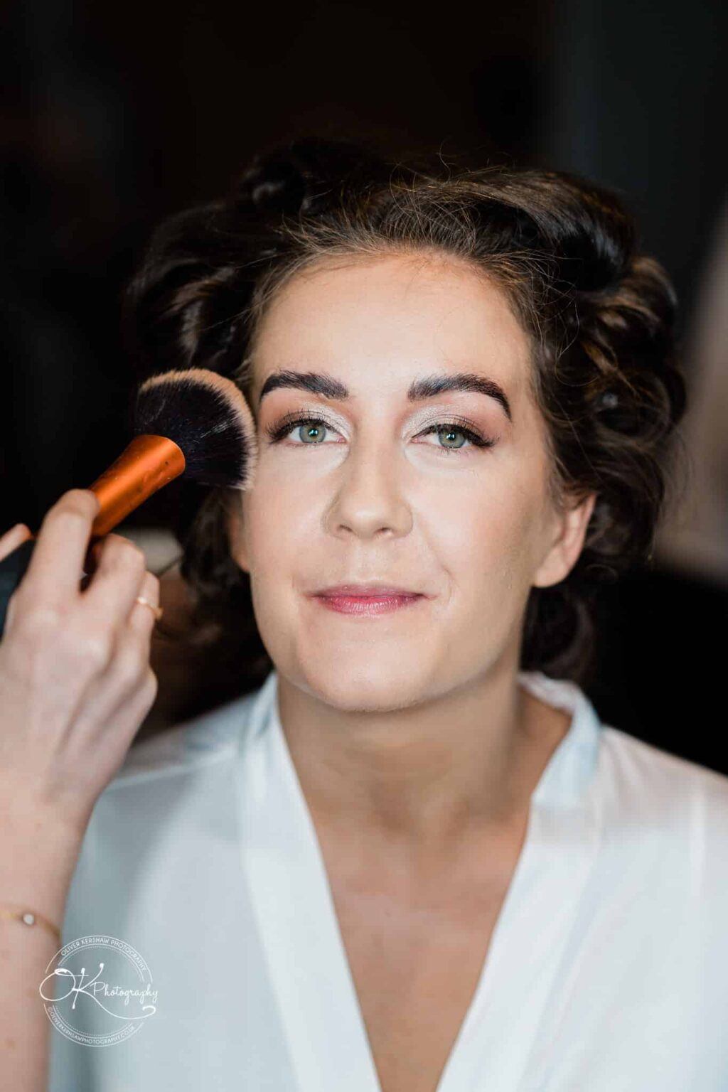 Warwick House Wedding Photography A close-up of a woman having makeup applied to her face with a brush.