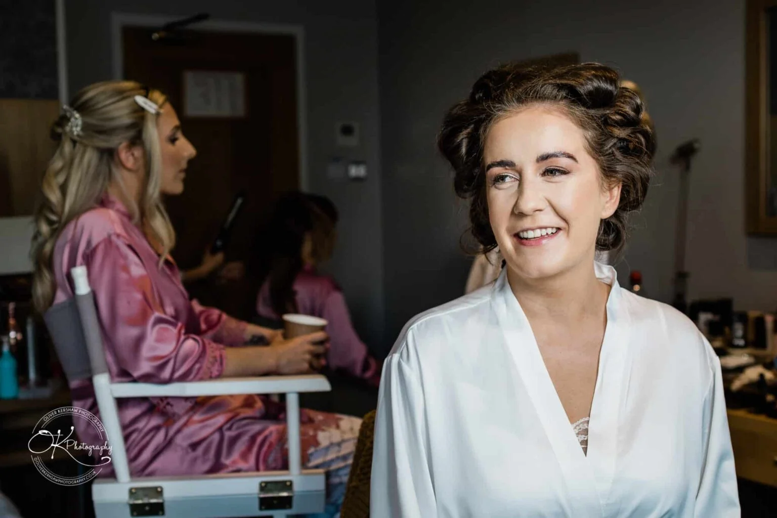 Warwick House Wedding Photography Bride getting ready in a dressing room with bridesmaids in the background.