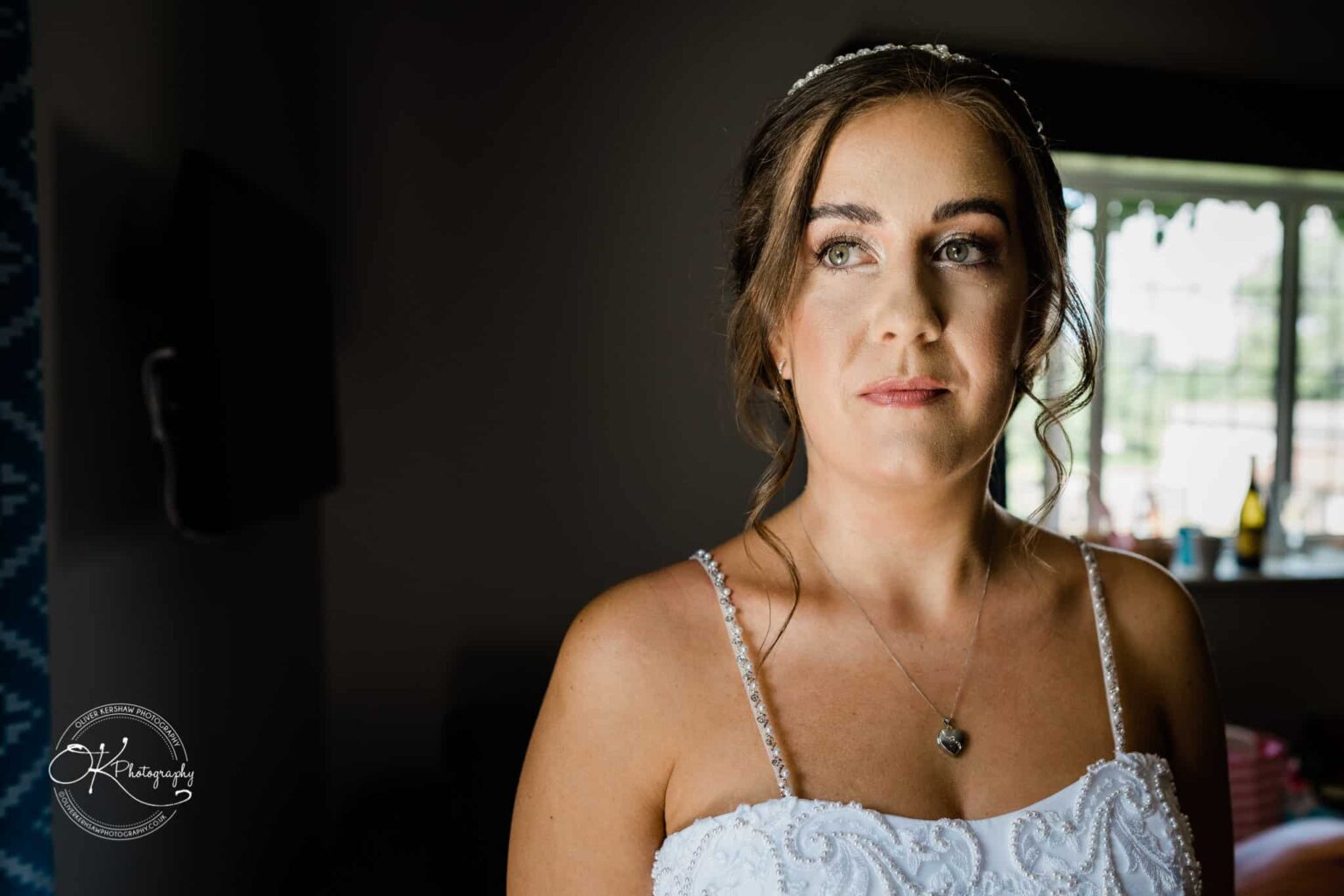 Warwick House Wedding Photography Bride in white wedding dress and tiara looking to the side, illuminated by natural light from a window at Warwick House.