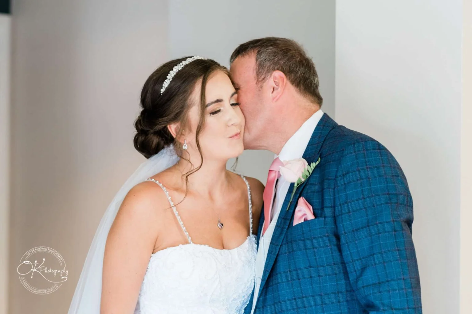 Warwick House Wedding Photography Bride and groom sharing a kiss, with the groom wearing a blue checked suit and the bride wearing a white dress with a tiara and veil.
