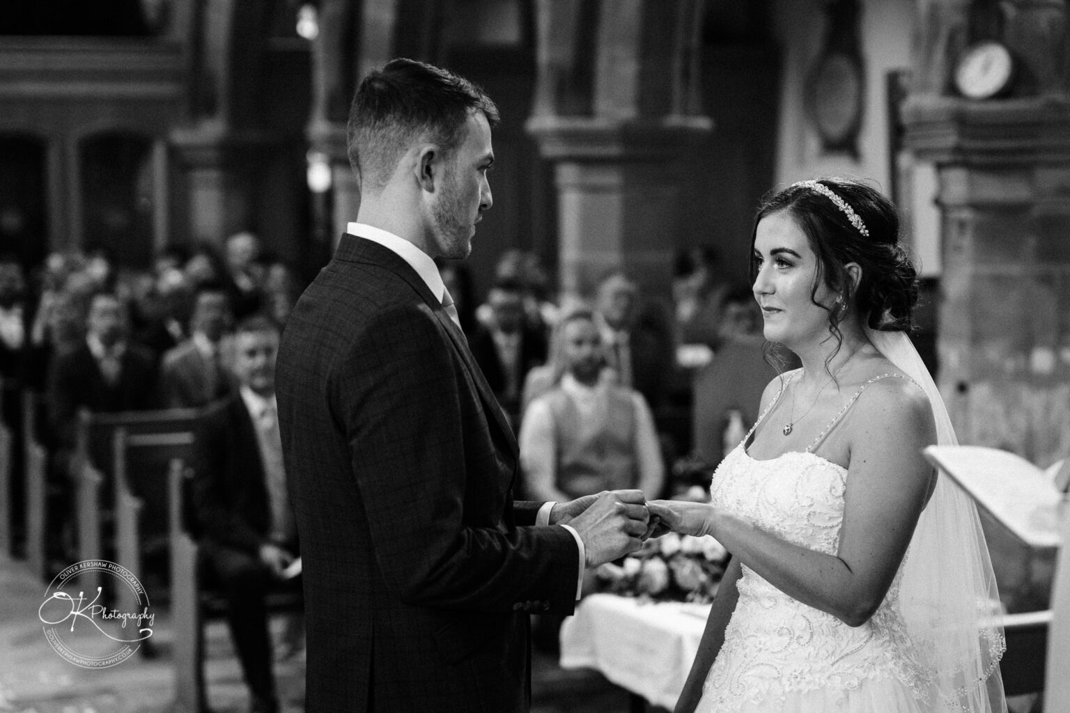 Warwick House Wedding Photography Bride and groom exchanging rings during a wedding ceremony in a church, with guests seated in the background.