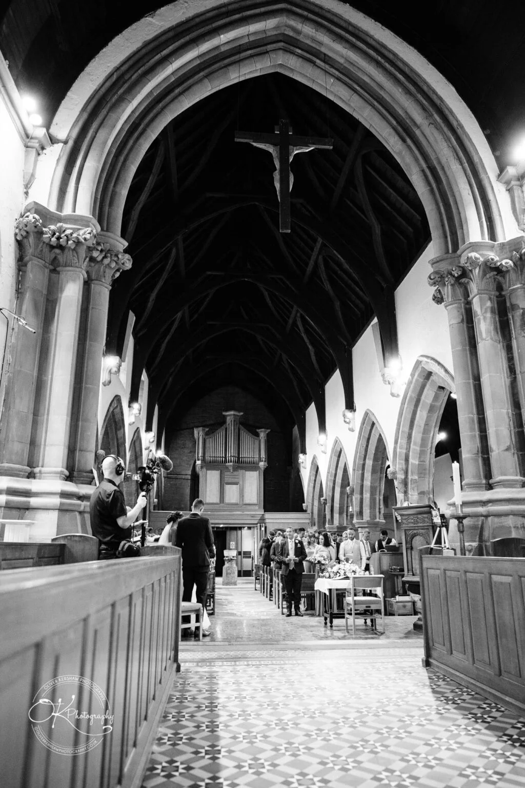 Warwick House Wedding Photography A black-and-white photograph of a church interior during a wedding ceremony, with a videographer filming the event.