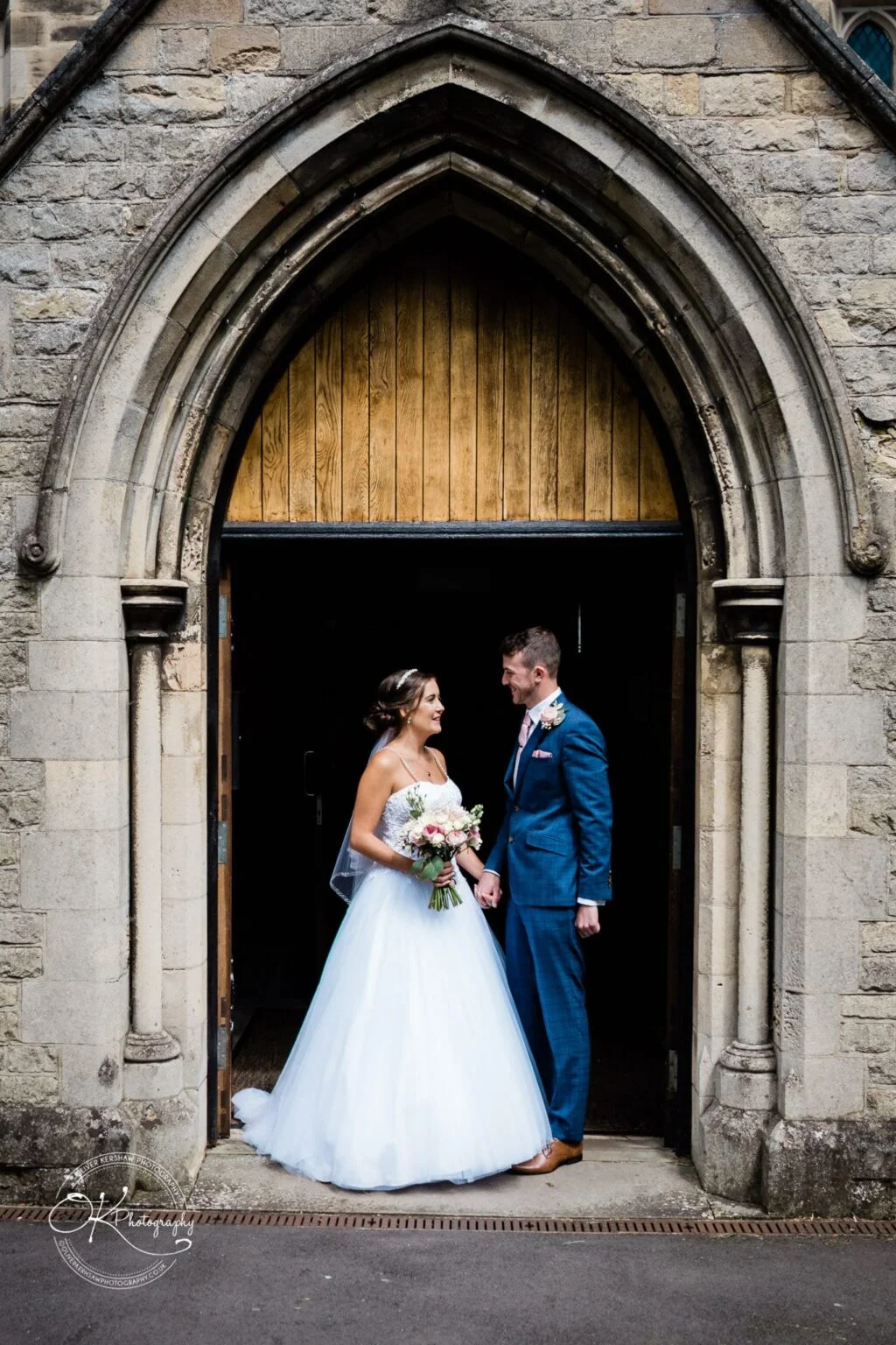 Warwick House Wedding Photography Bride and groom standing at the entrance of a stone building with an arched wooden door.