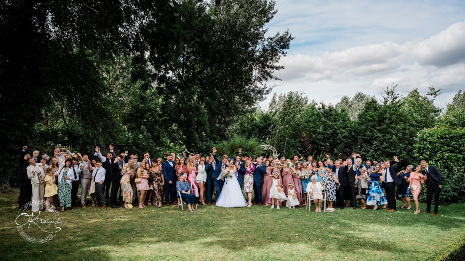 Warwick House Wedding Photography A large wedding party stands together on a lawn, surrounded by trees and greenery, at Warwick House.