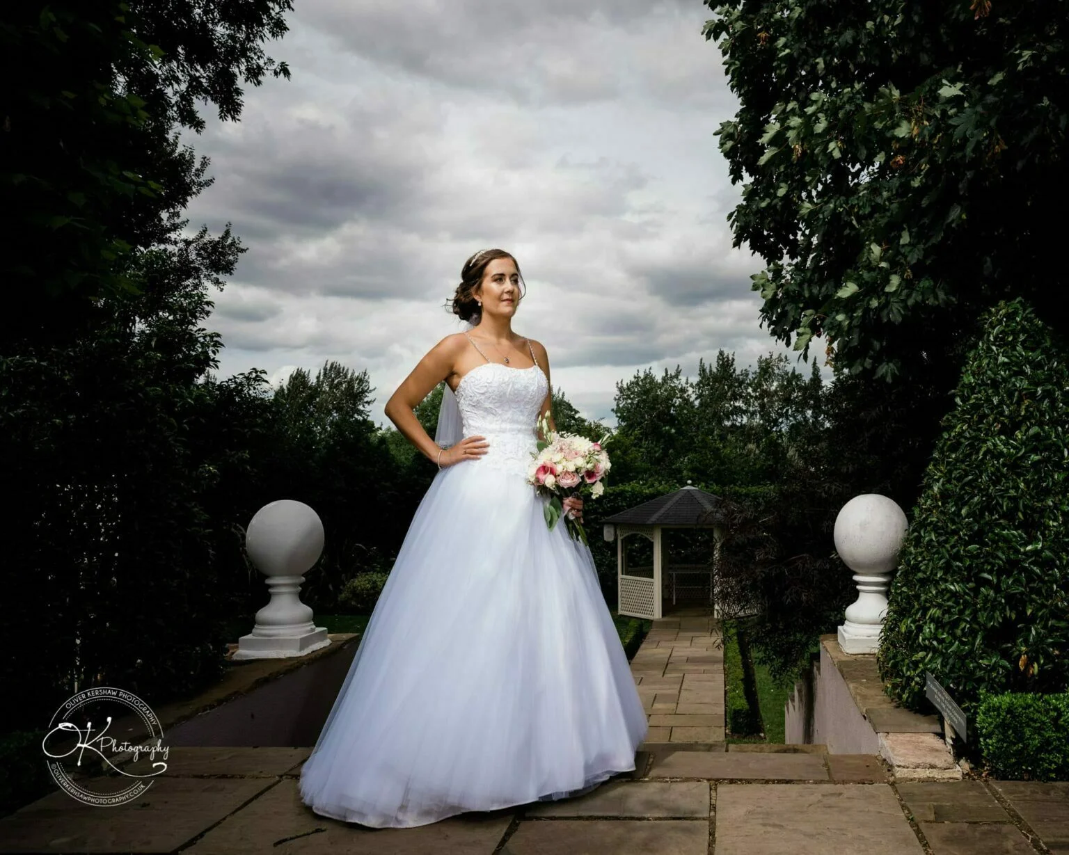 Warwick House Wedding Photography Bride in white wedding gown holding bouquet, standing on stone steps at Warwick House with greenery and gazebo in the background.