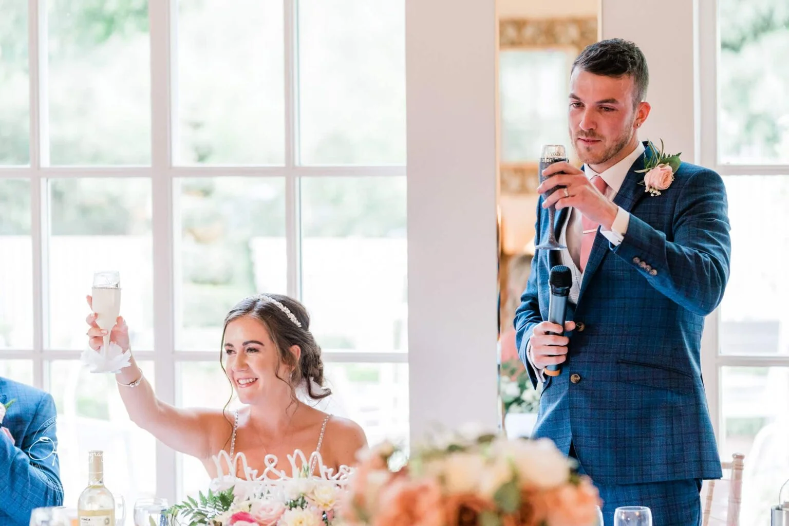 Warwick House Wedding Photography Wedding couple raising glasses for a toast at a reception, the groom holding a microphone while the bride smiles.