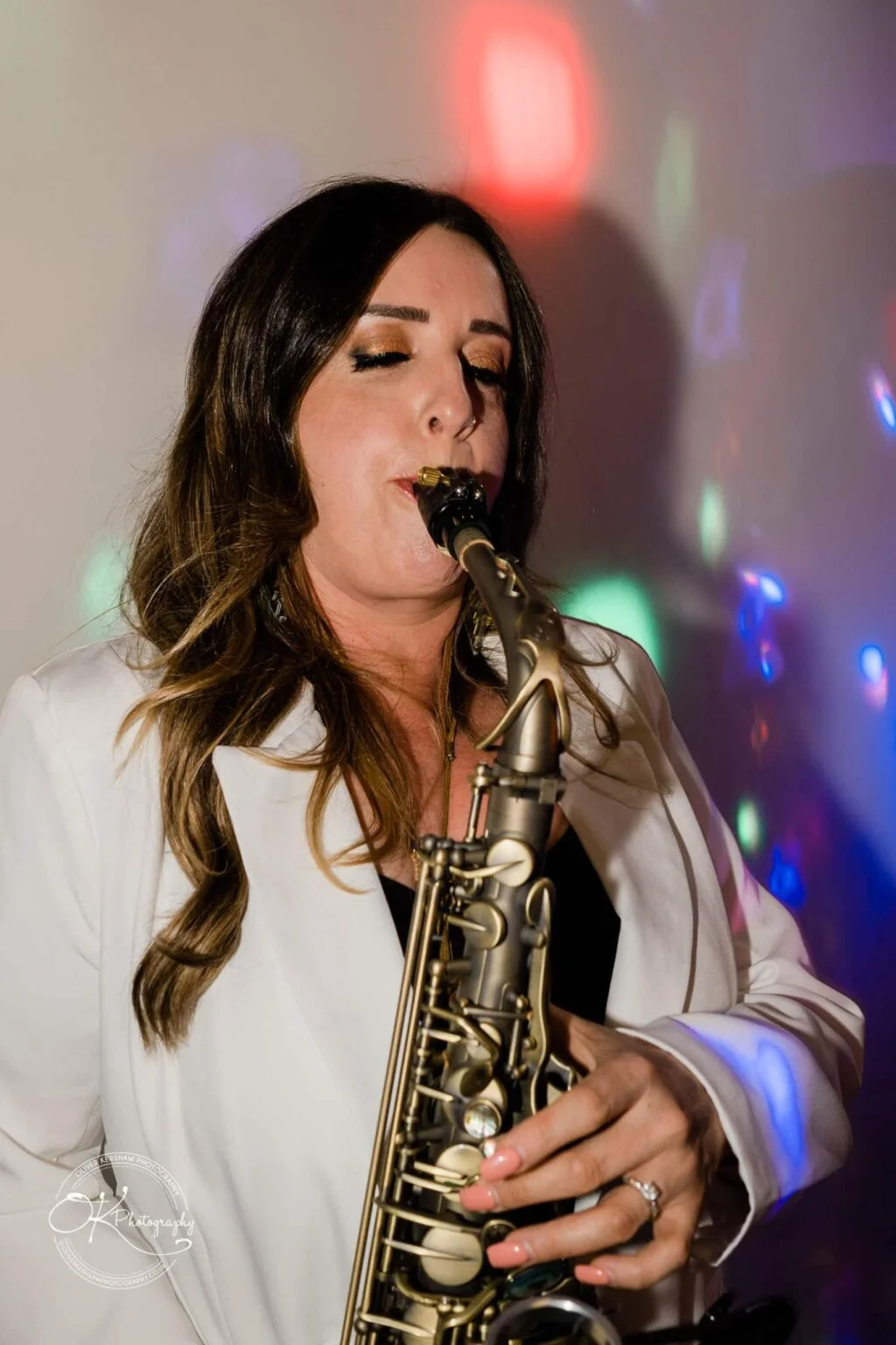 Warwick House Wedding Photography Woman playing a saxophone at a wedding, with colourful lights in the background.