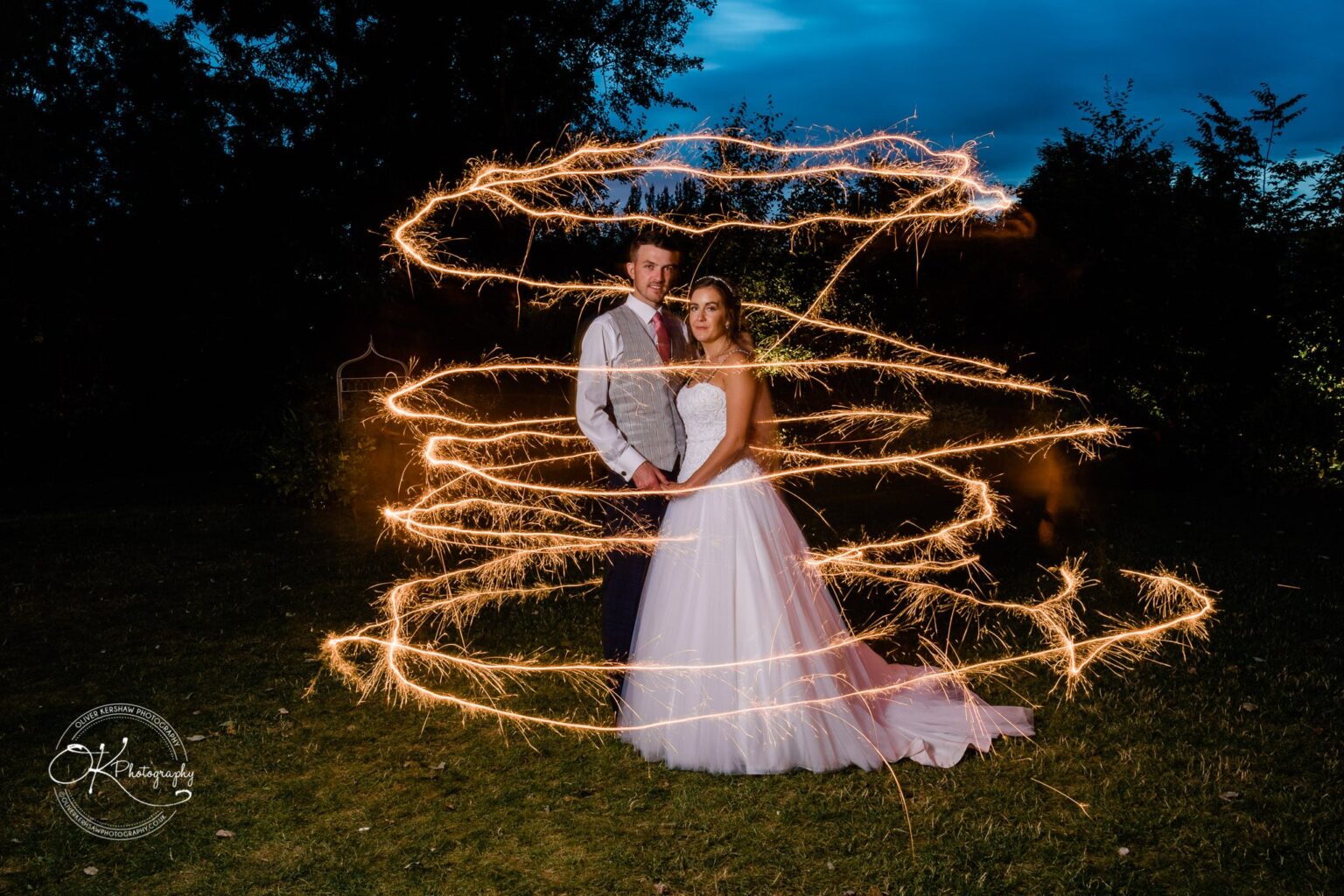 Warwick House Wedding Photography Bride and groom surrounded by swirling sparklers, standing outside at night