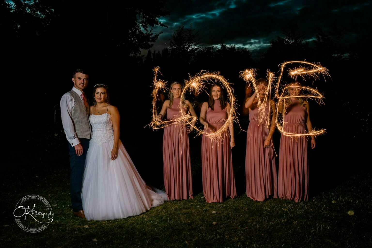 Warwick House Wedding Photography Bride and groom standing with bridesmaids holding sparklers that spell "LOVE" against a dark background.