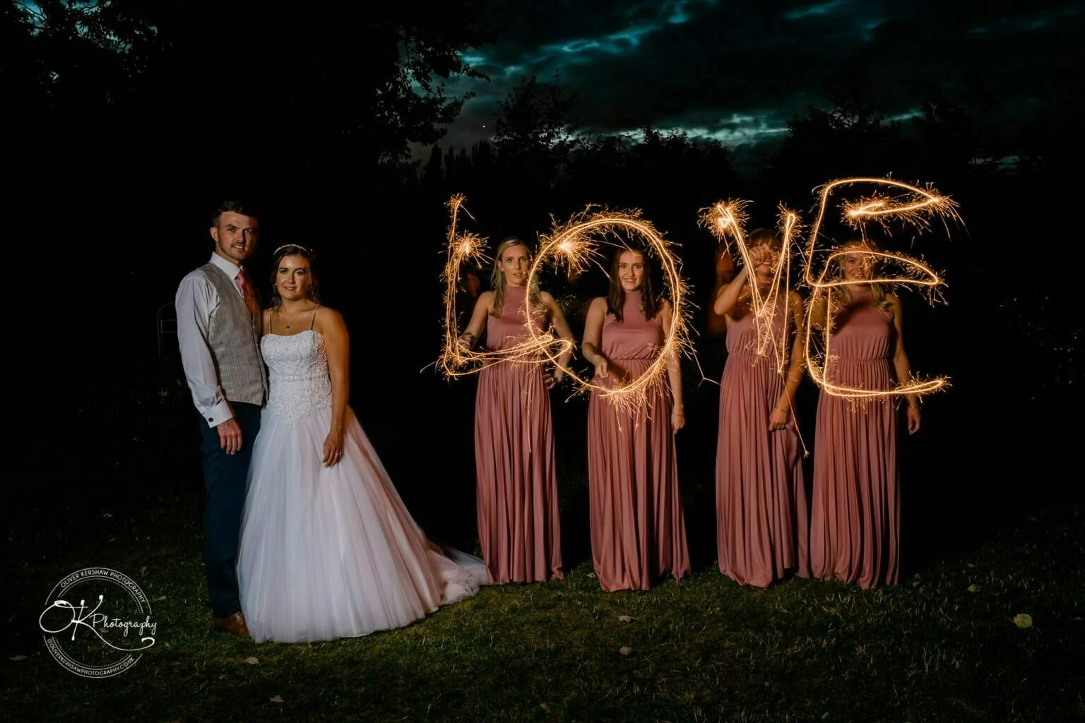 Warwick House Wedding Photography Bride and groom standing with bridesmaids holding sparklers that spell "LOVE" against a dark background.