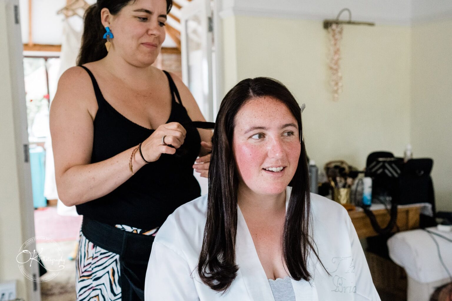 Wedding photography St Michael & All Angels Church A woman is styling another woman's hair indoors, preparing her for an event.
