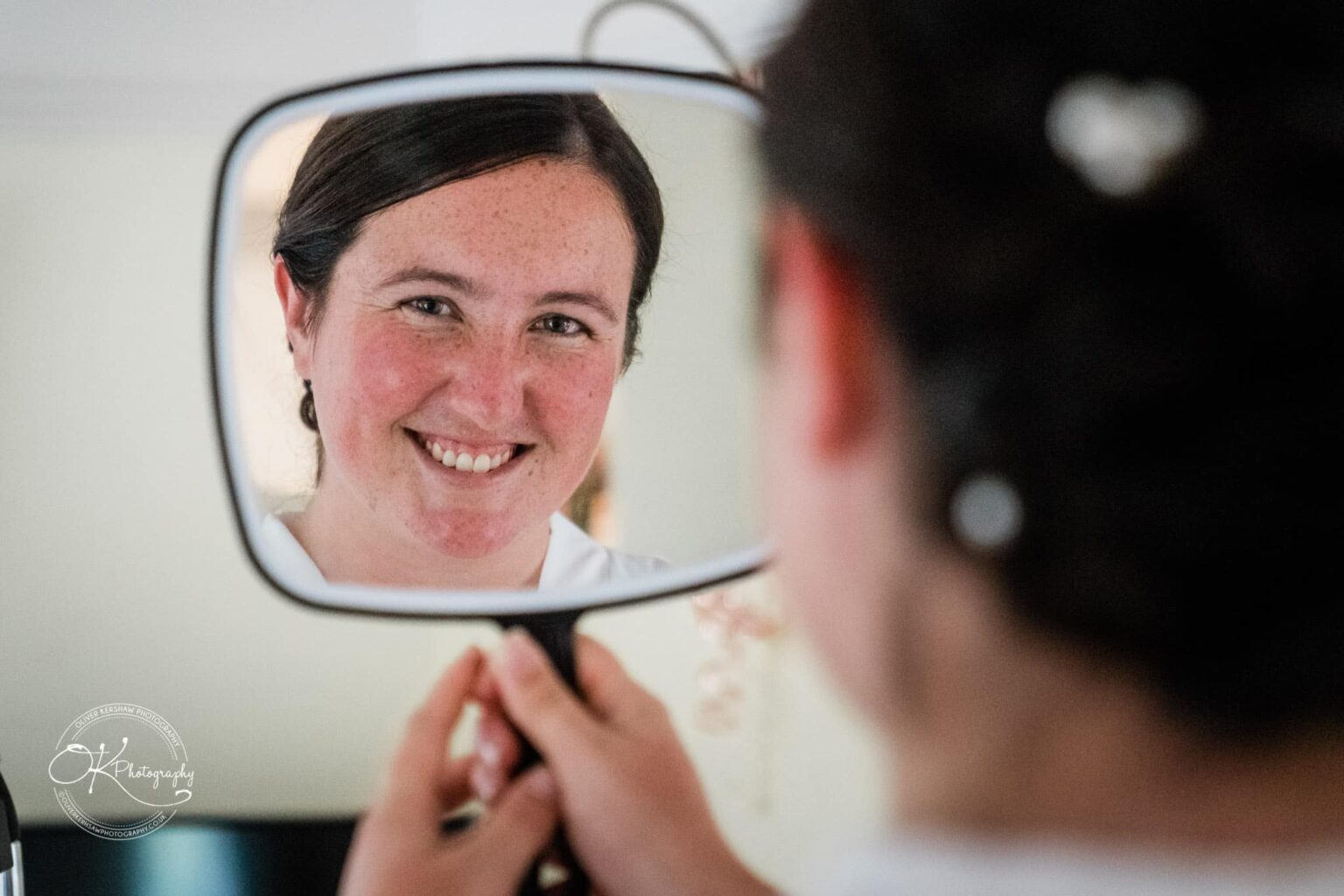 Wedding photography St Michael & All Angels Church A woman smiling while looking at her reflection in a hand-held mirror.