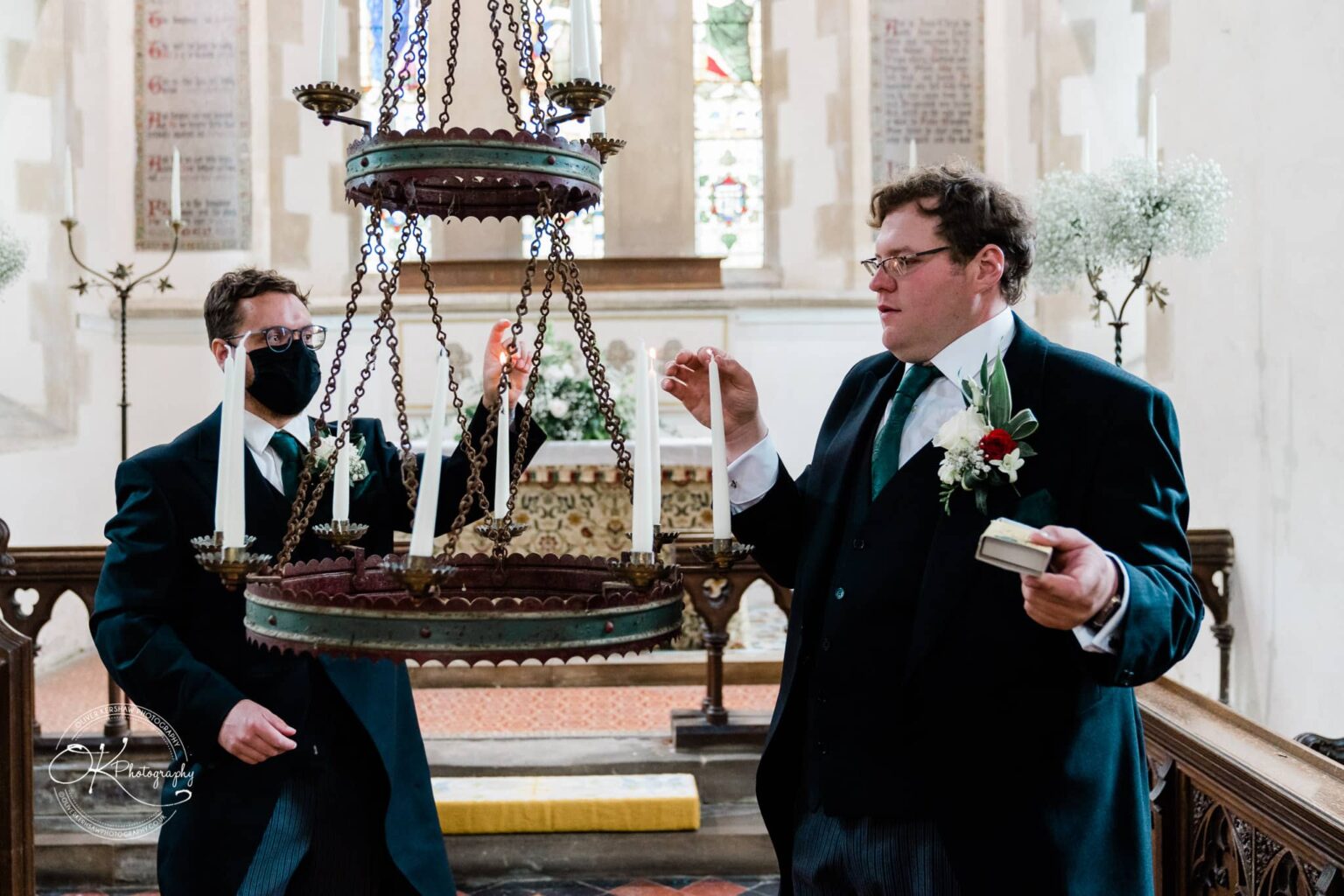 Wedding photography St Michael & All Angels Church Two men in formal attire lighting candles in a chandelier inside St. Michael Church.