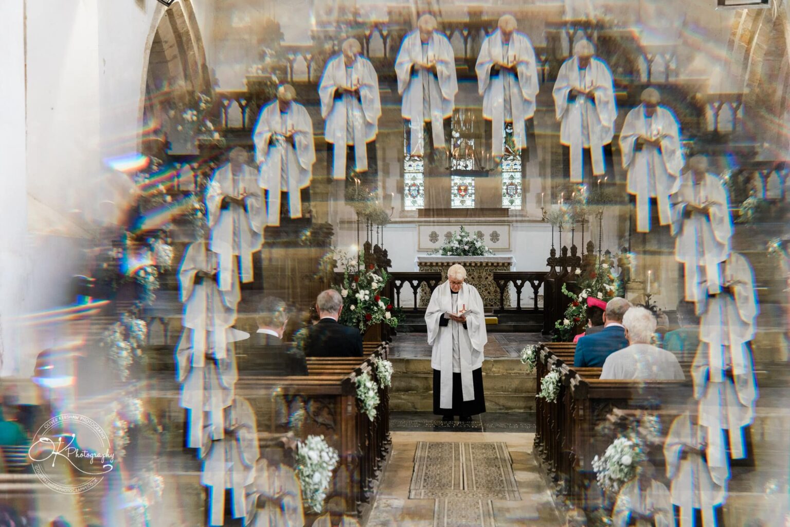 Wedding photography St Michael & All Angels Church A priest stands at the altar in St Michael church, with multiple reflections of him surrounding the scene. Several people are seated in pews, and the altar is decorated with flowers.