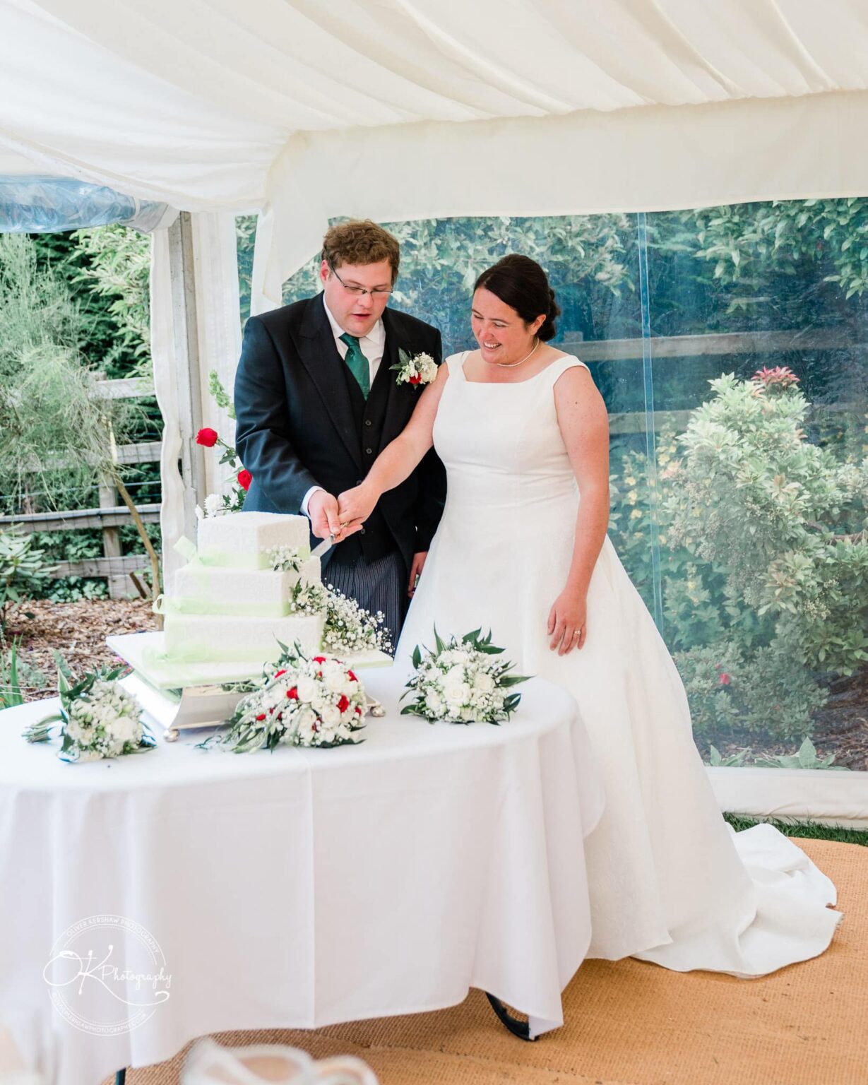 Wedding photography St Michael & All Angels Church A bride and groom cutting their wedding cake under a white canopy, surrounded by floral arrangements.