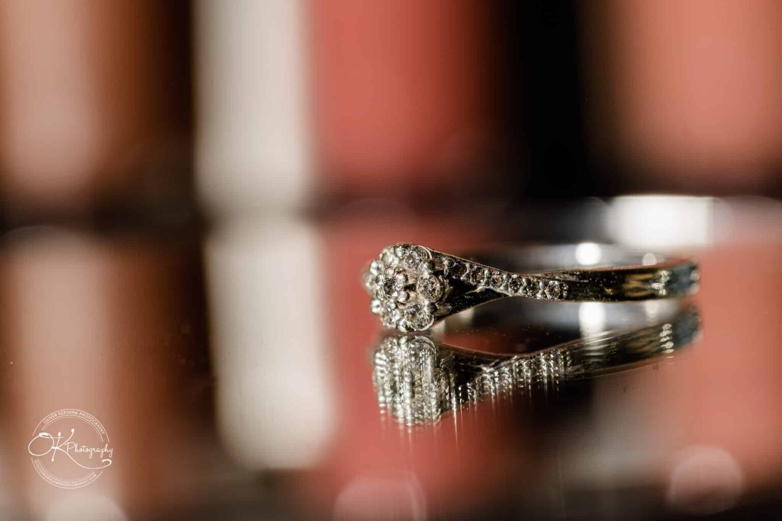 Wedding photography The Embankment A close-up of a diamond ring with a floral design, reflecting on a smooth surface against a blurred background.