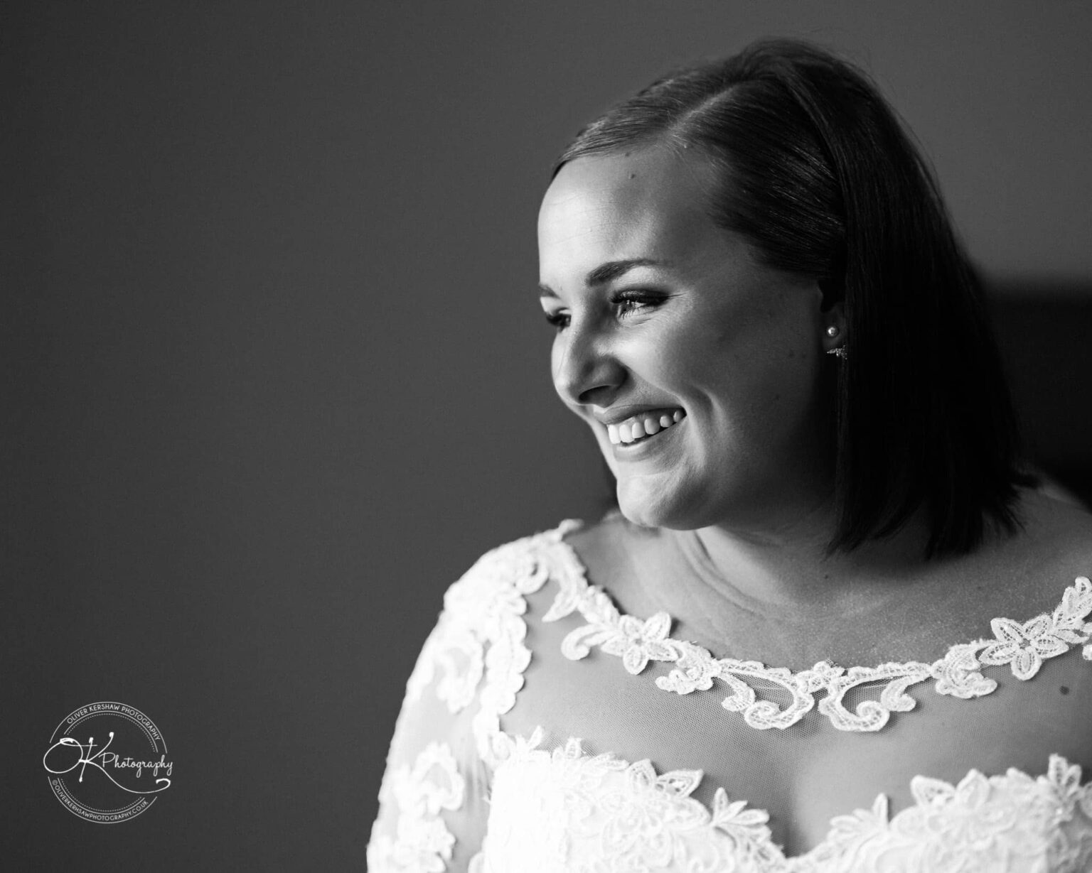 Wedding photography The Embankment Black and white portrait of a smiling woman in a wedding dress with lace details, looking to the right.