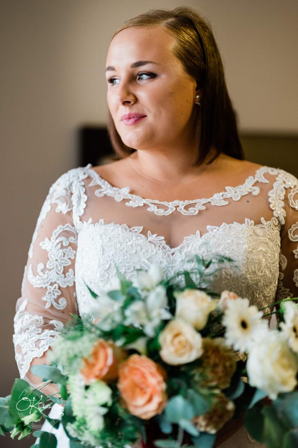 Wedding photography The Embankment A bride in a lace wedding dress holds a bouquet of flowers, gazing to the side.