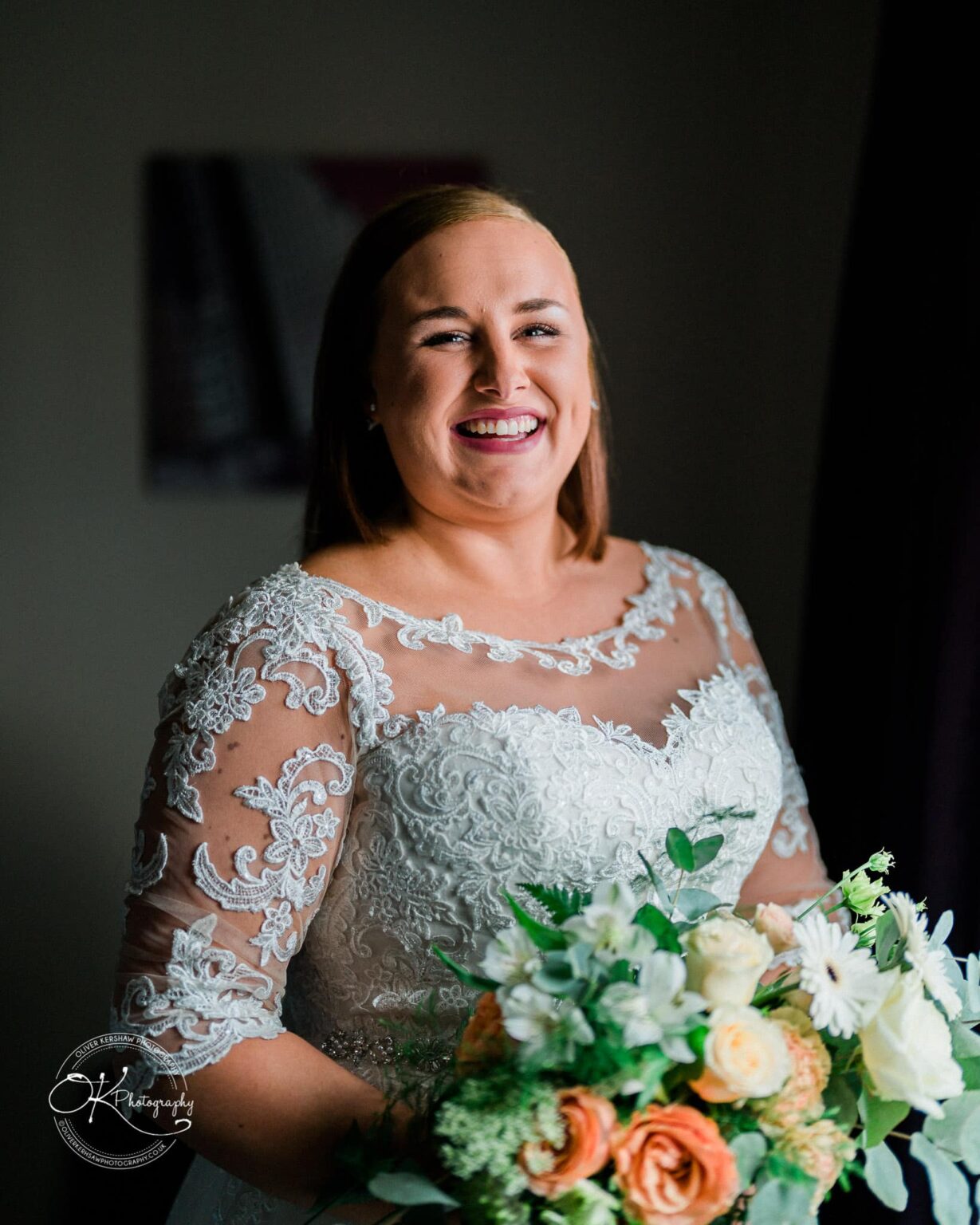 Wedding photography The Embankment A bride in a lace wedding dress holding a bouquet of flowers, smiling at the camera.