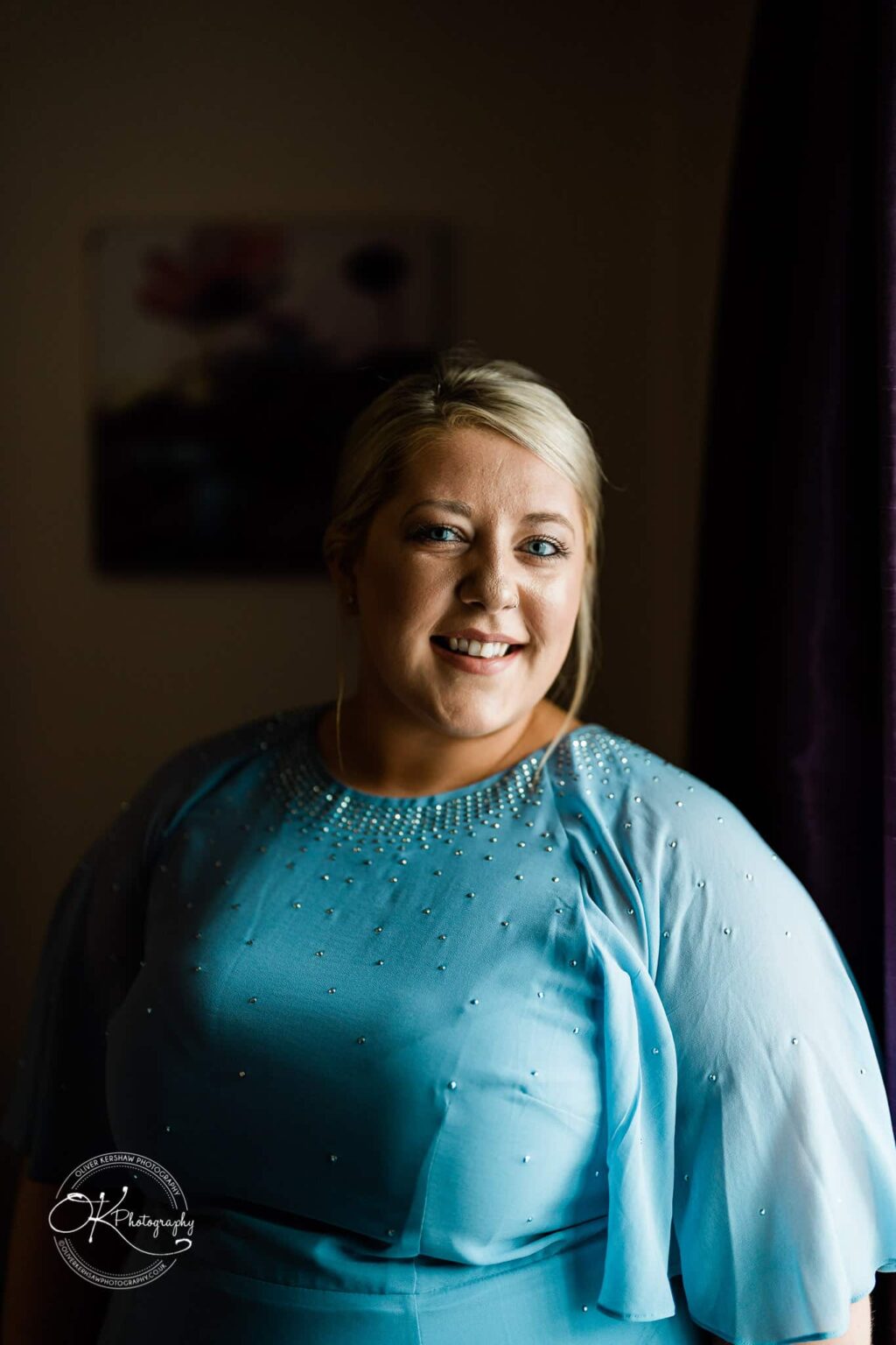 Wedding photography The Embankment Woman smiling, wearing a light blue dress with embellishments, standing indoors.