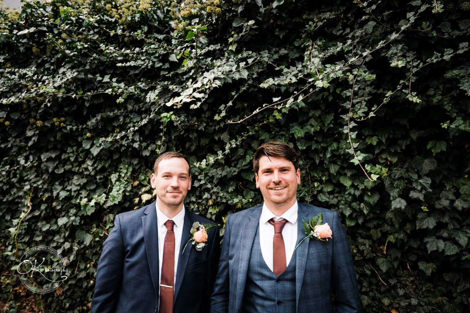 Wedding photography The Embankment Two men dressed in suits with boutonnieres standing in front of a green ivy-covered wall.
